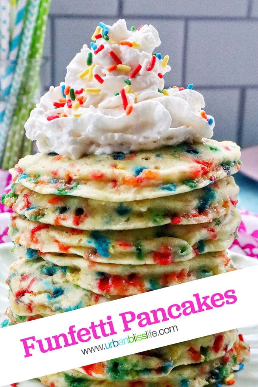 huge stack of funfetti pancakes with whipped cream and sprinkles on a scalloped green plate.