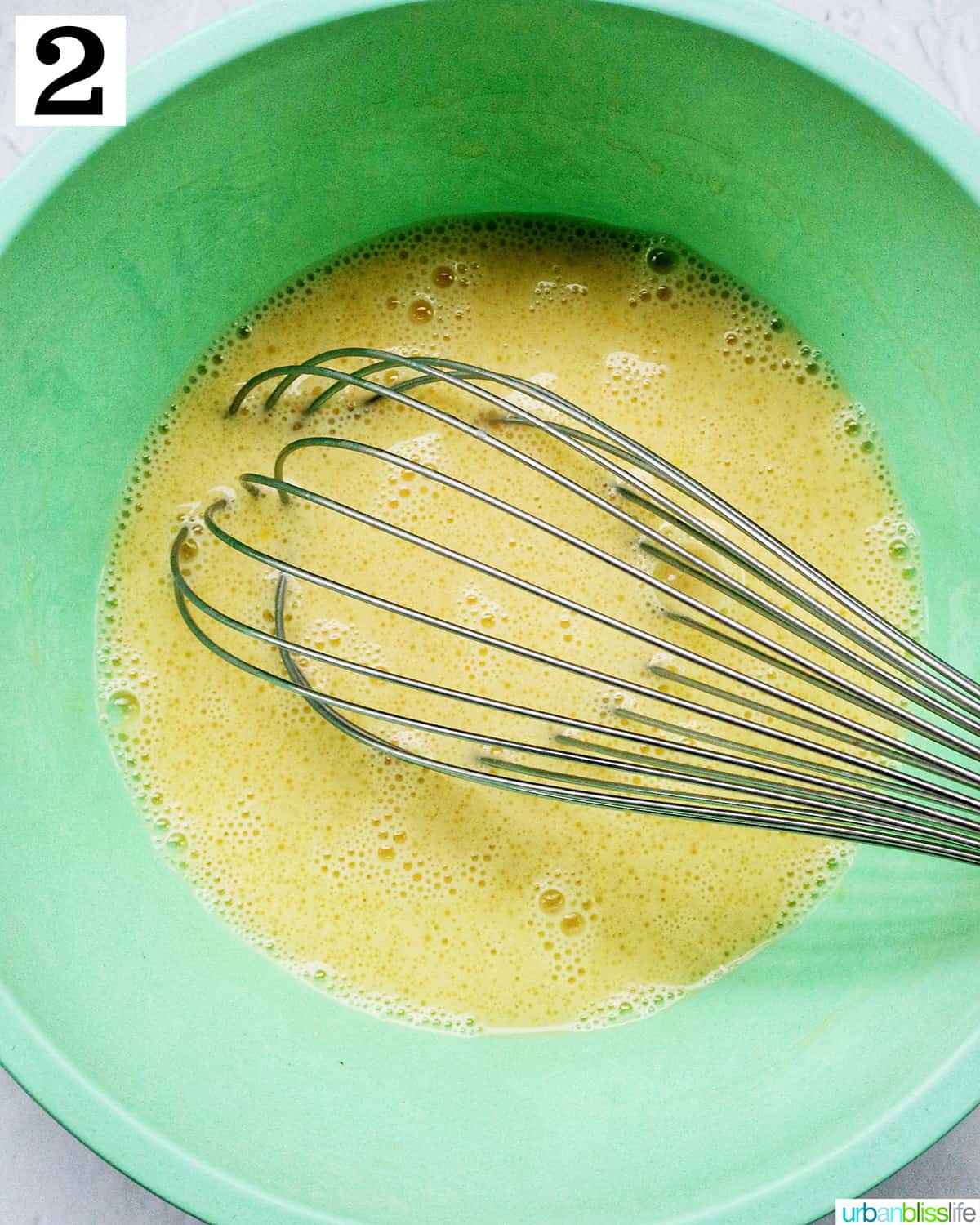 large green bowl with wet ingredients and a whisk.