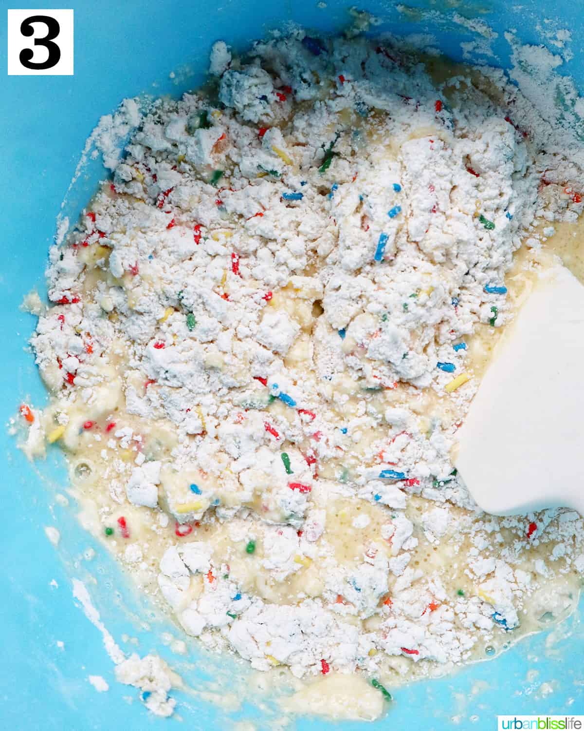 large bluw mixing bowl with ingredients to make funfetti pancakes with a spatula.