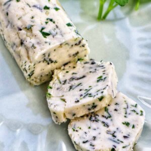 garlic herb compound butter on a green plate with side of herbs.