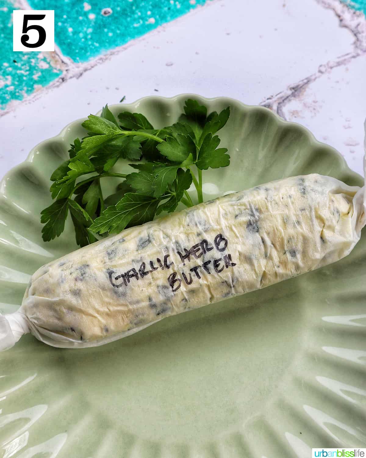 garlic herb compound butter on a green plate with side of herbs.