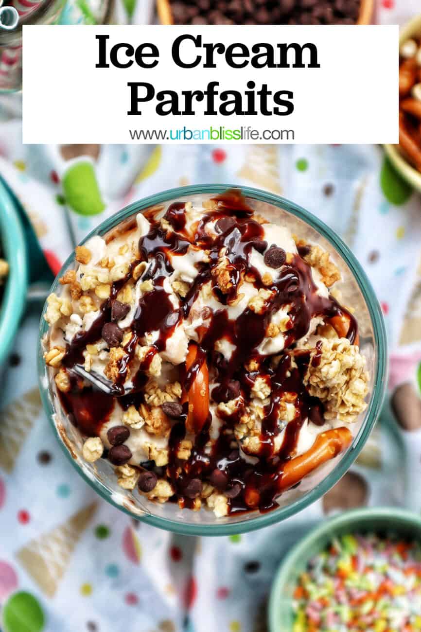 ice cream parfait topped with granola, chocolate syrup, mini chocolate chips on a colorful kitchen towel surrounded by sides of more toppings.
