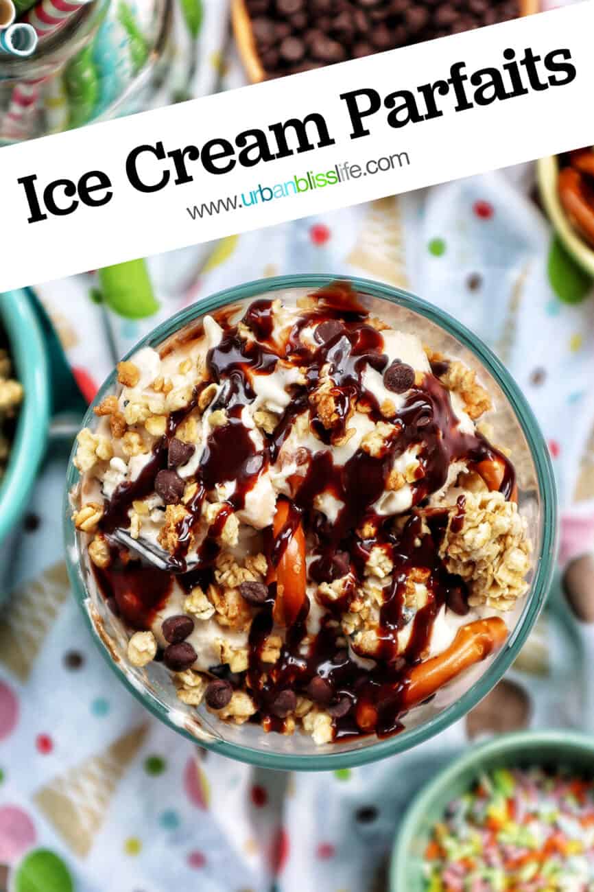 ice cream parfait topped with granola, chocolate syrup, mini chocolate chips on a colorful kitchen towel surrounded by sides of more toppings.