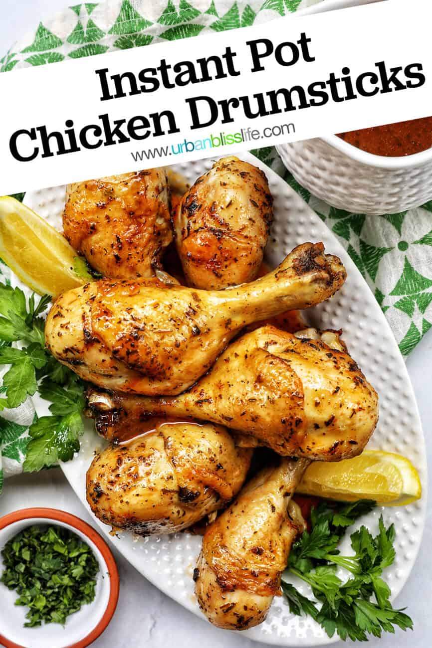 Stack of chicken drumsticks with seasoning and garnished with parsley and side of lemon wedges on bed of herbs.