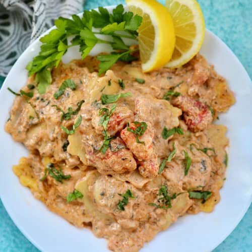 lobster ravioli sauce with lobster meat, lemon wedges, and herbs in a white bowl.