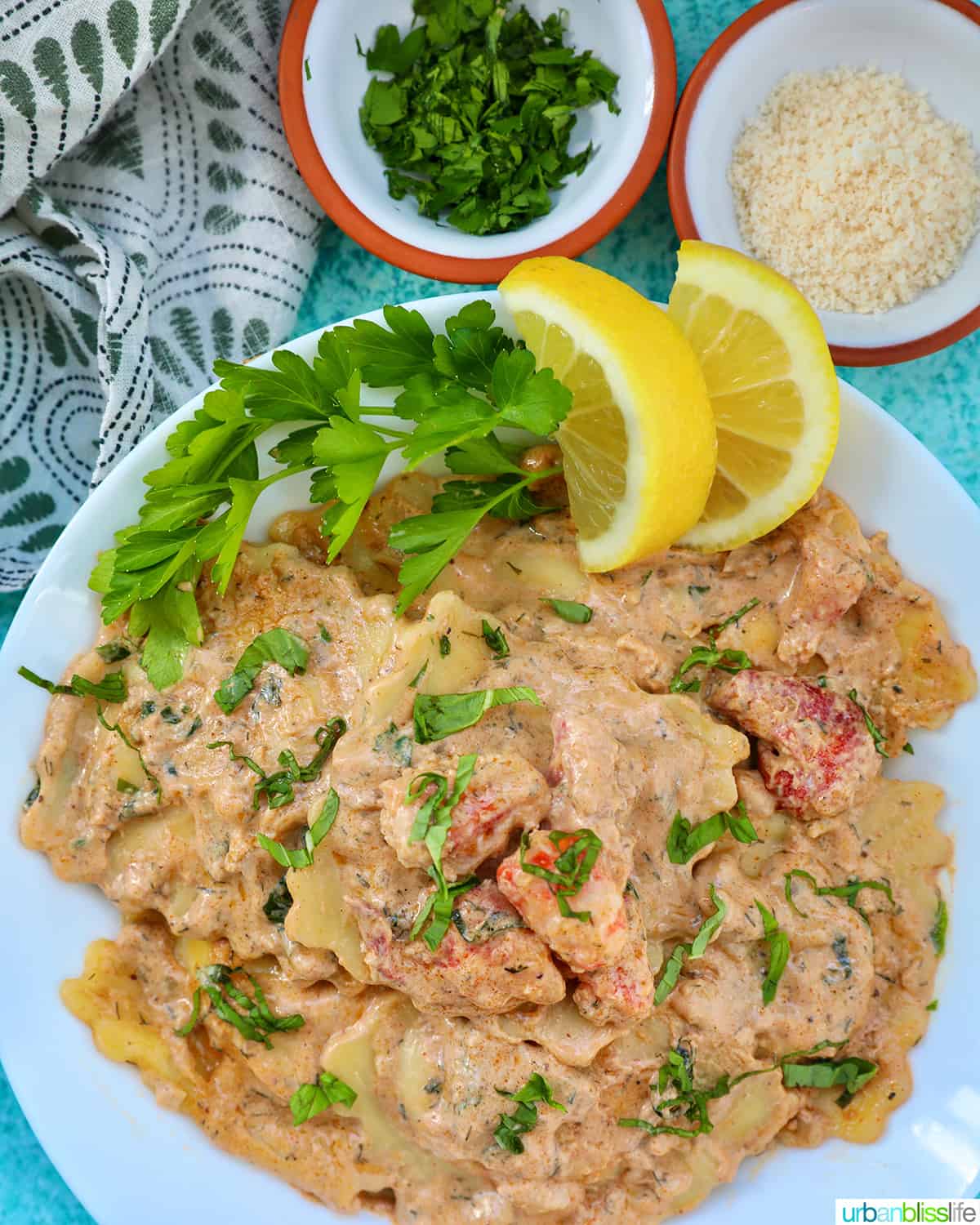 lobster ravioli sauce with lobster meat, lemon wedges, and herbs in a white bowl.