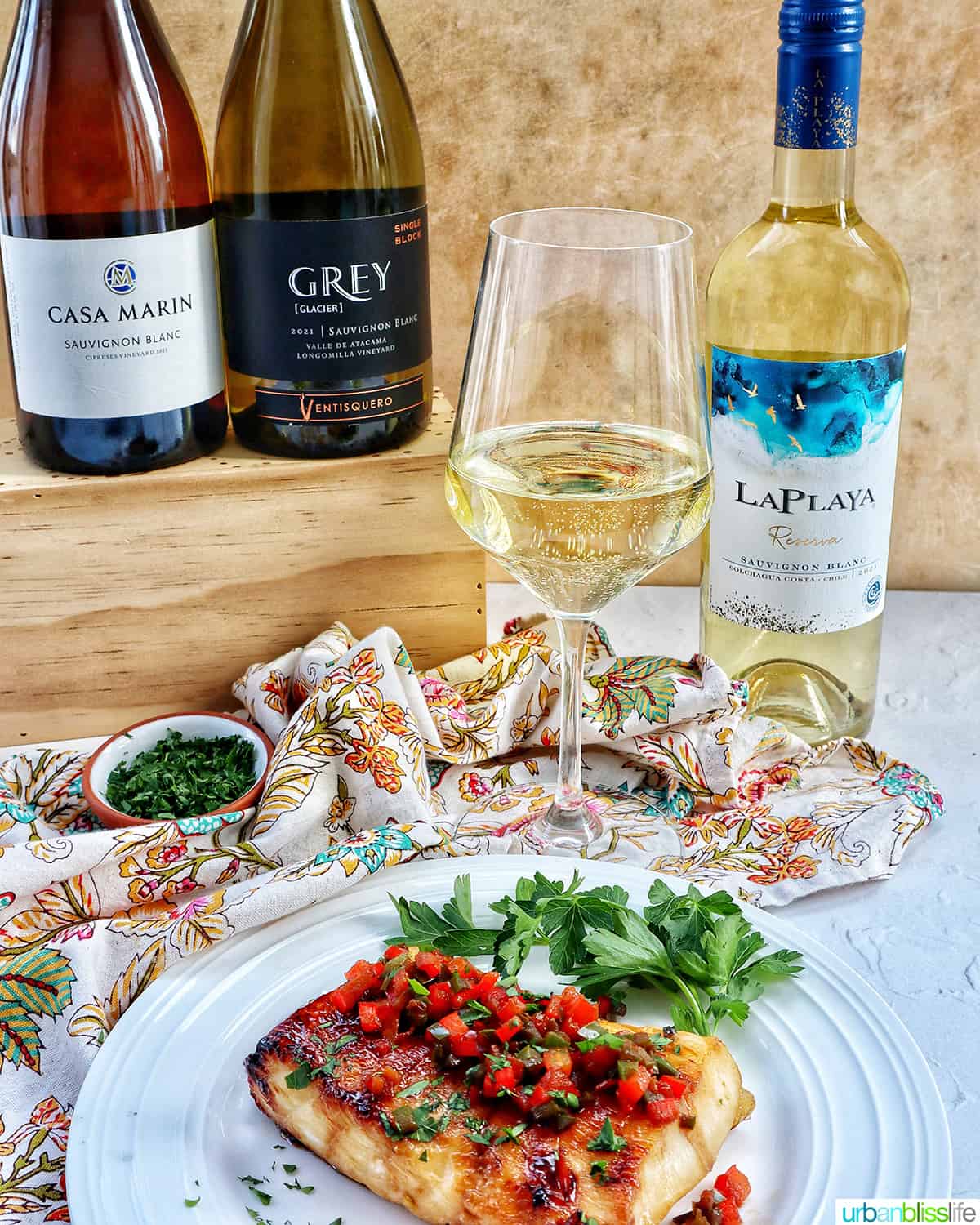 three bottles of wine and a glass of sauvignon blanc white wine behind a plate of pan seared Chilean sea bass.
