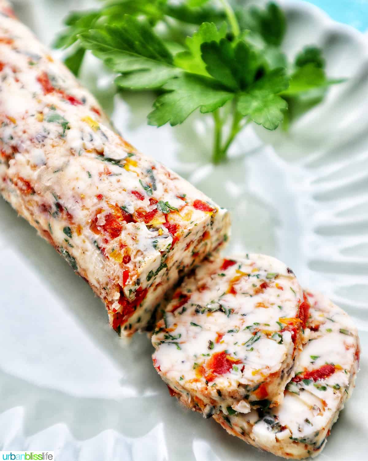 slices of sun dried tomato butter on a green plate with side of herbs.