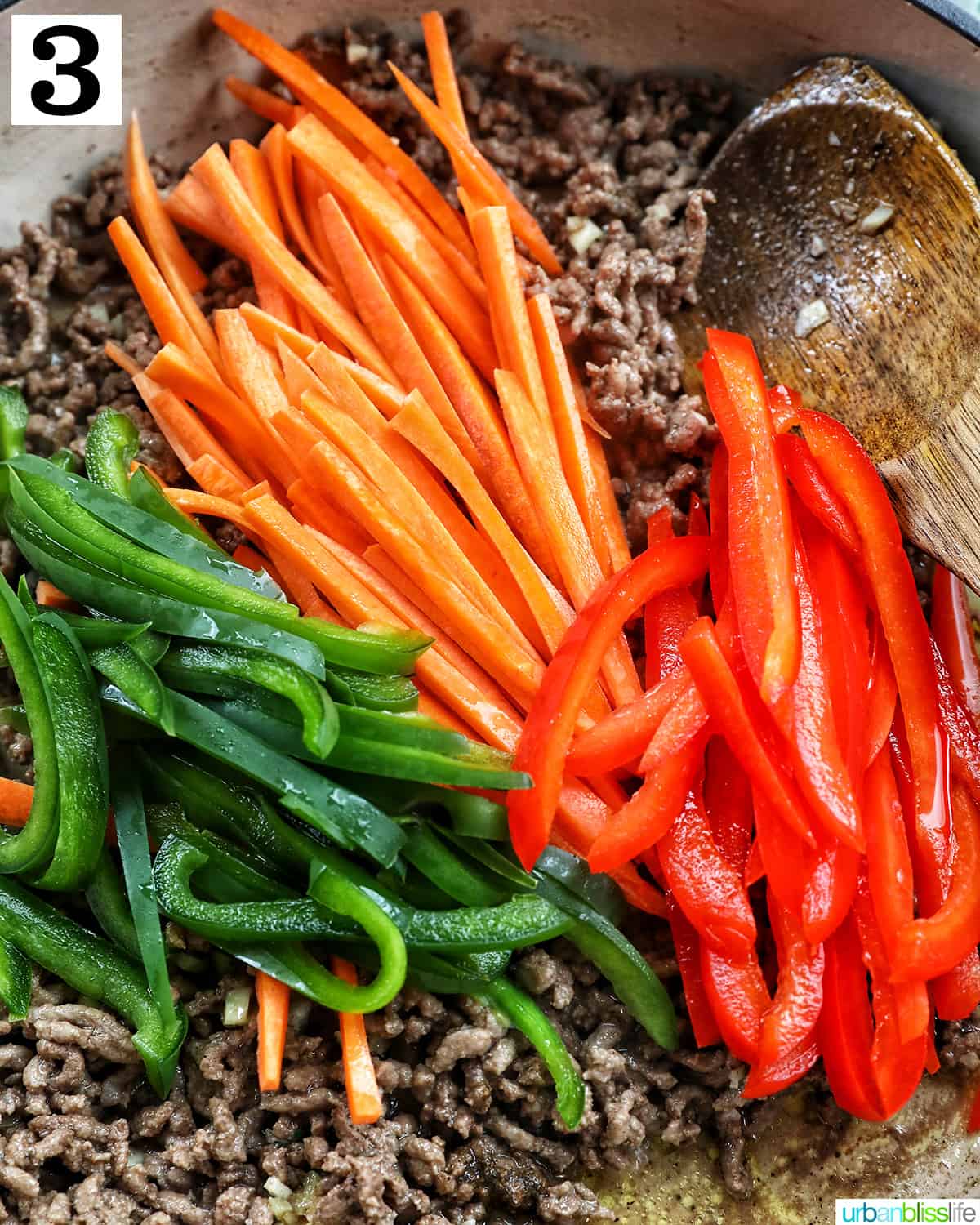 sliced carrots, red bell pepper, green bell pepper over ground beef in a skillet.