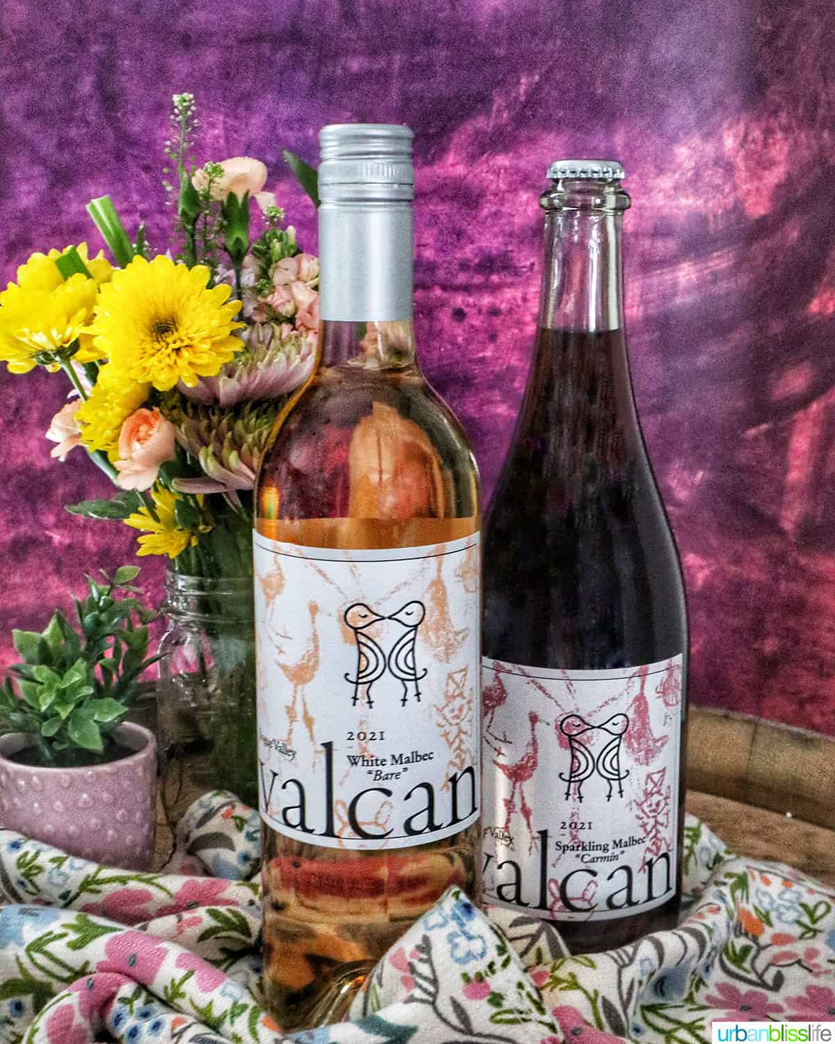 Valcan Cellars bottle of White Malbec and Sparkling Malbec on spring towel on a wine barrel with spring flowers.