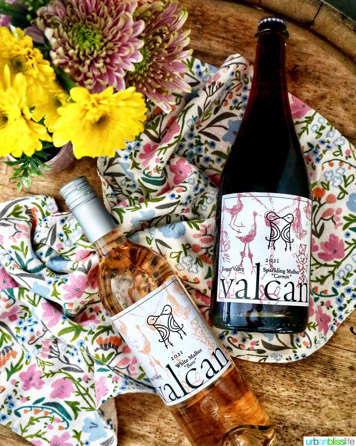 Valcan Cellars bottle of White Malbec and Sparkling Malbec on spring towel on a wine barrel with spring flowers.