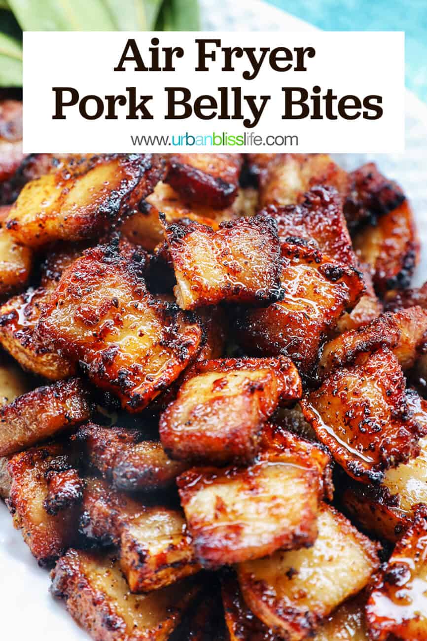 pile of air fryer pork belly bites on a white serving platter with bay leaves on a blue background with title text that reads Air Fryer Pork Belly Bites.