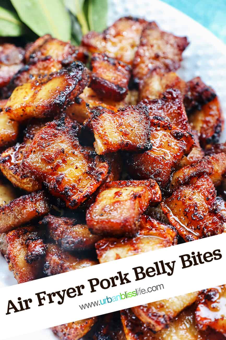 pile of air fryer pork belly bites on a white serving platter with bay leaves on a blue background with title text that reads Air Fryer Pork Belly Bites.