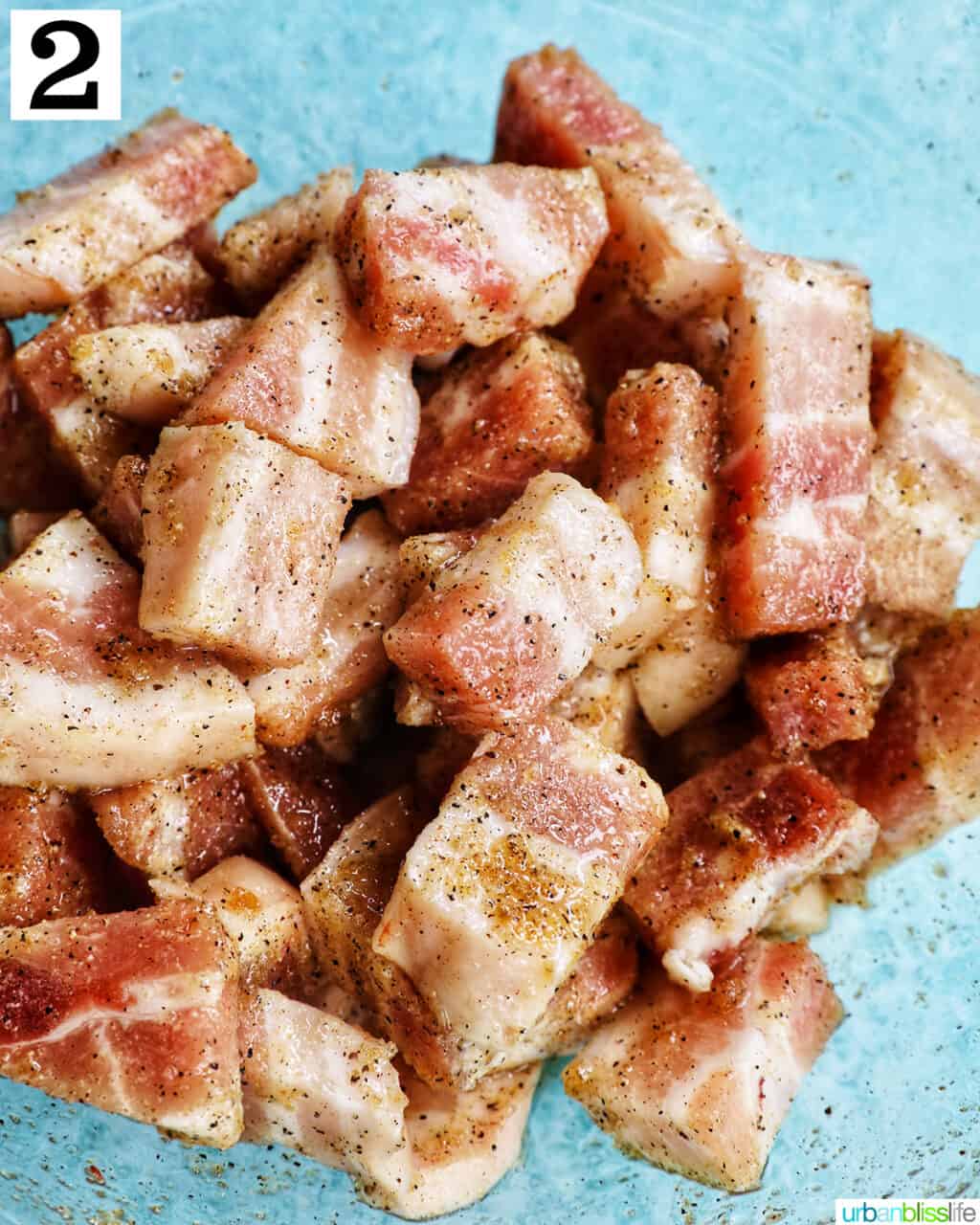 pork belly bites seasoned in a glass bowl over blue background.