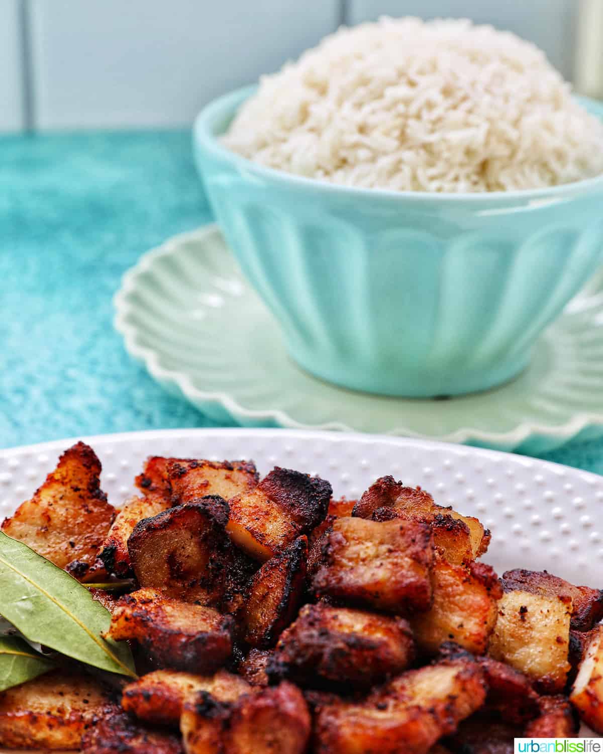 plate of air fryer pork belly bites (lechon kawali) in the foreground with a blue bowl filled with white rice in the background.
