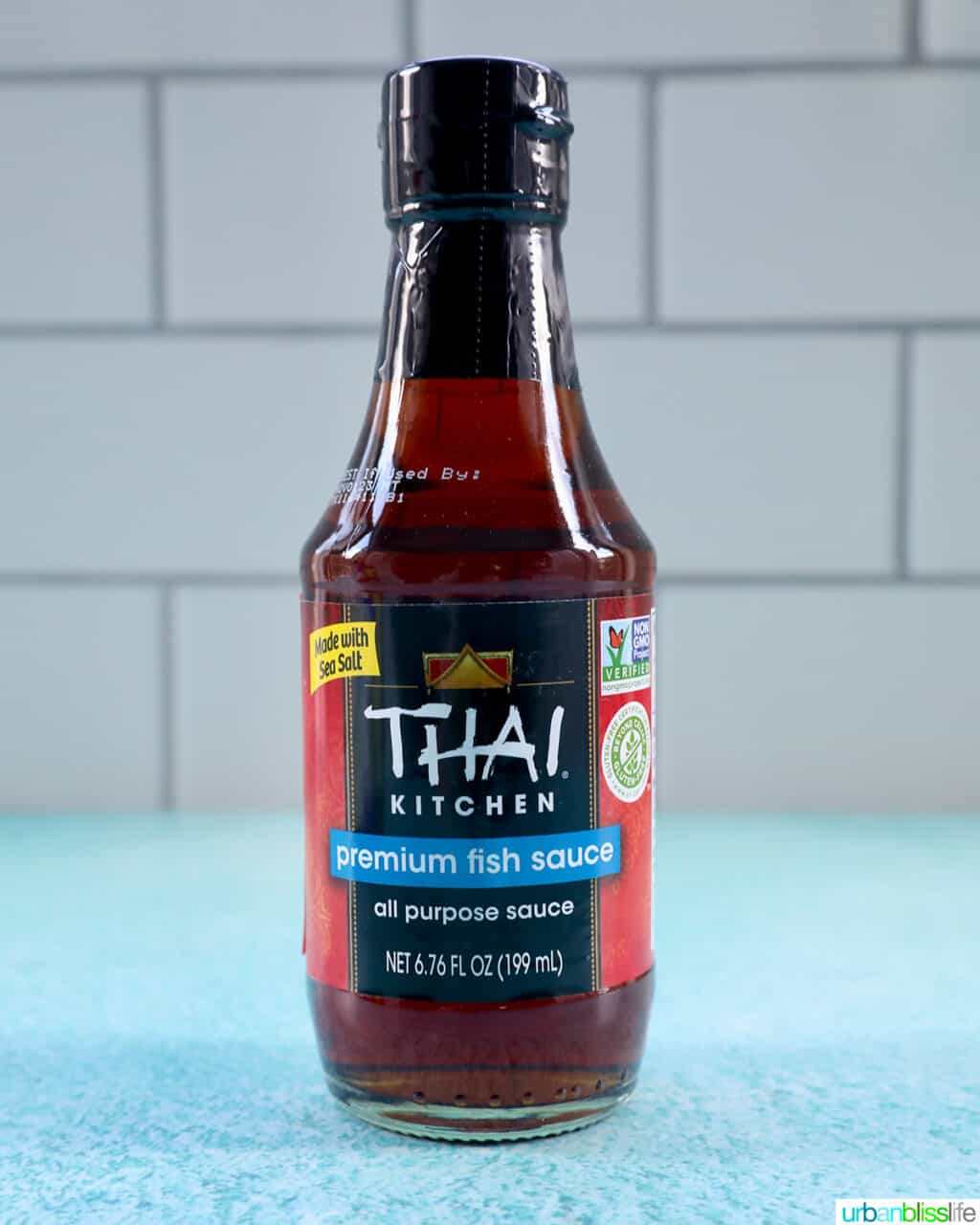 bottle of Thai kitchen fish sauce on a bright blue table with kitchen tile background.
