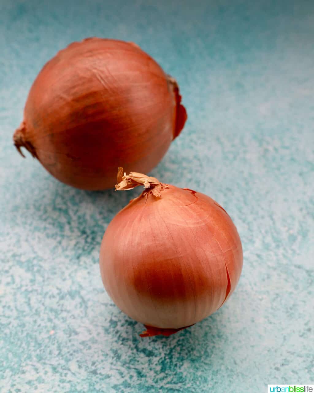 two yellow onions on a blue table with white tile background.
