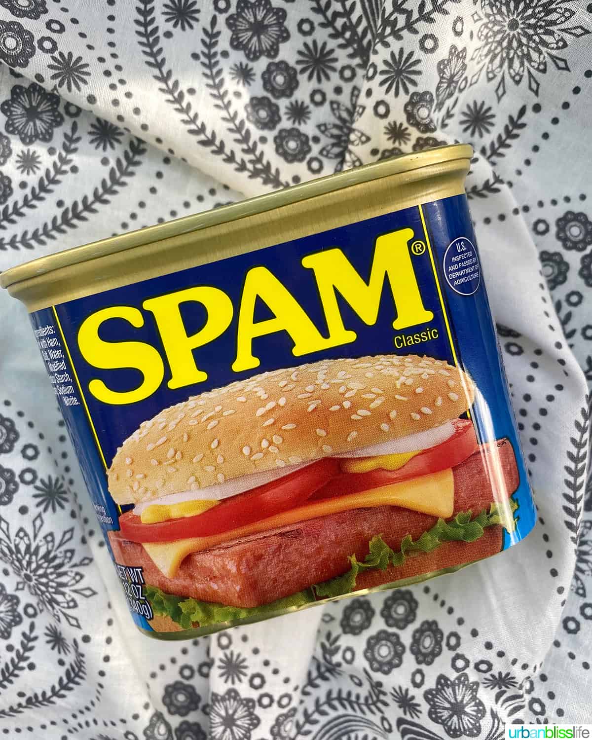 can of SPAM on a white and grey floral tablecloth.
