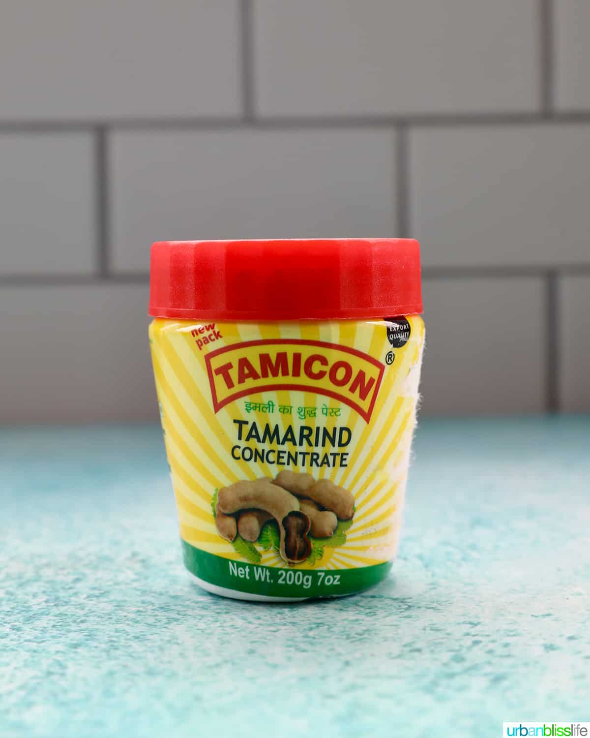 jar of tamarind paste on a blue table with white tile background.