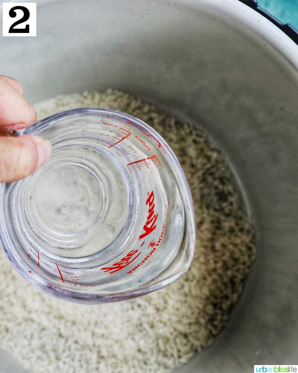 hand holding a pyrex measuring cup of water over an instant pot pot with white rice.