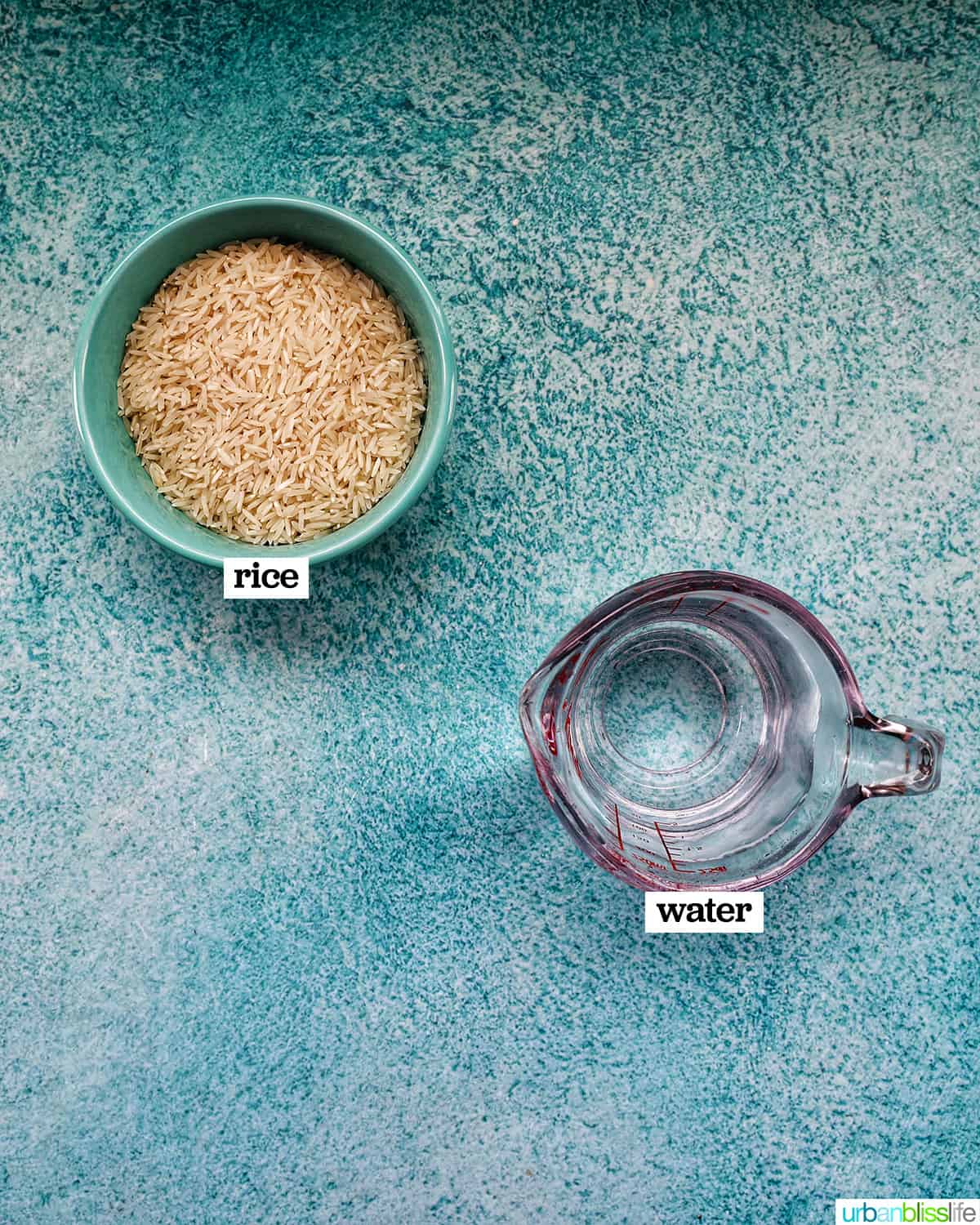 basmati rice in a blue bowl next to a pyrex measuring cup of water on a blue background.