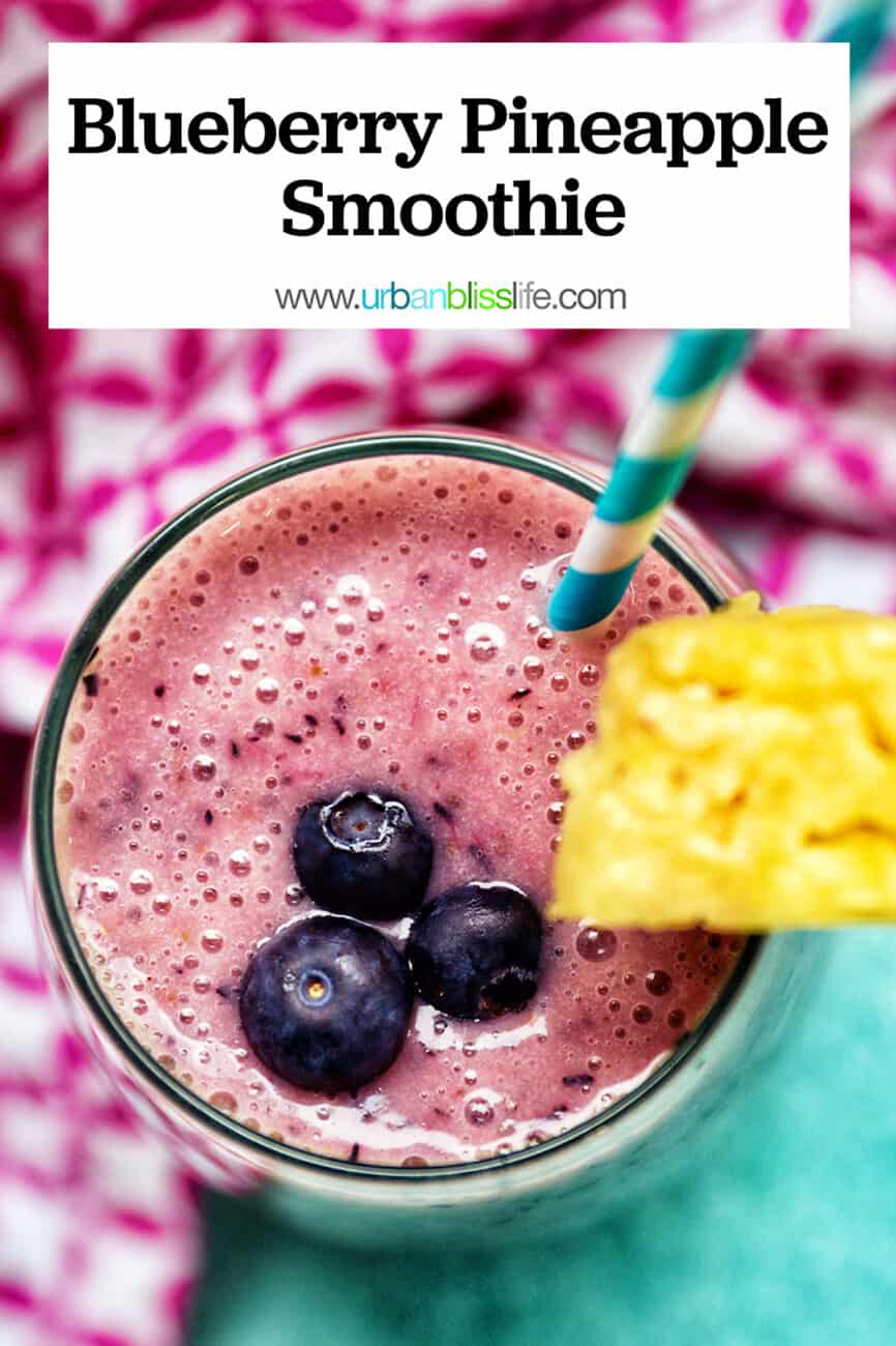 glass of Blueberry Pineapple Smoothie with pineapple wedge garnish, blue and white stripe straw, and pink and white napkin.