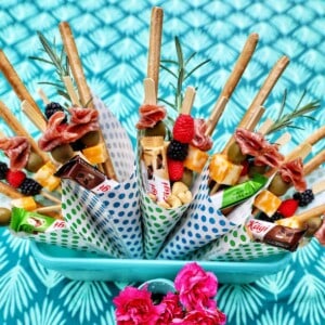 Charcuterie cones with fruit, cheeses, breadsticks, nuts, chocolate, herbs in paper cones.