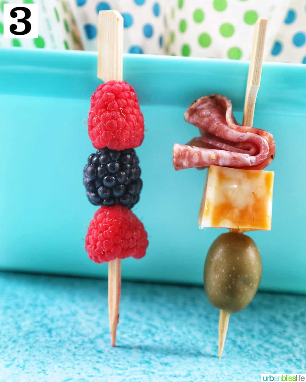 food skewer with salami, cheese, and olives and a food skewer with fruit.