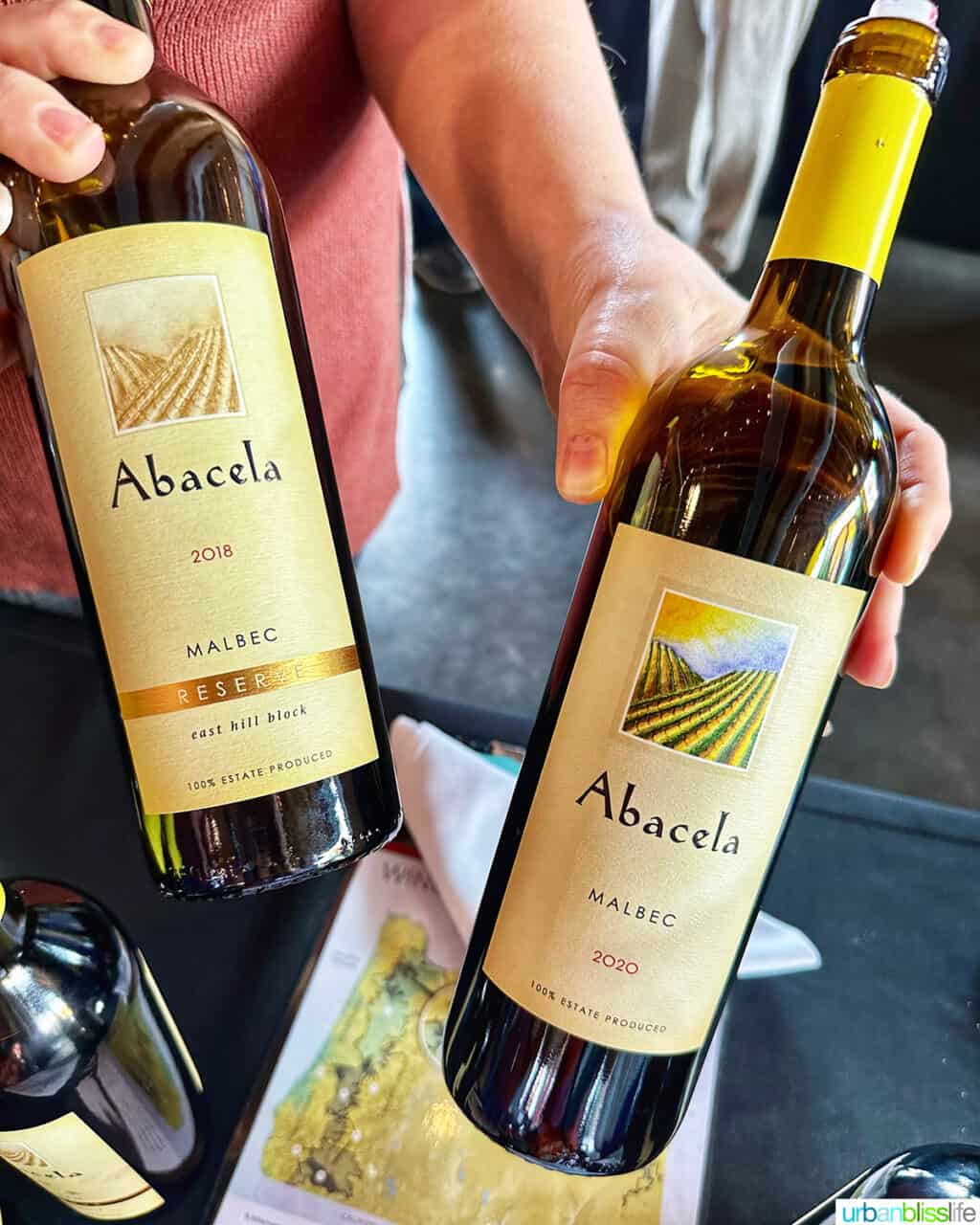 hands holding two bottles of Abacela malbec wines.