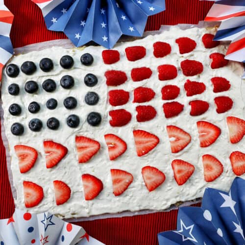 4th of July Fruit Pizza with blueberries, strawberries, raspberries surrounded by red, white, and blue decorations.