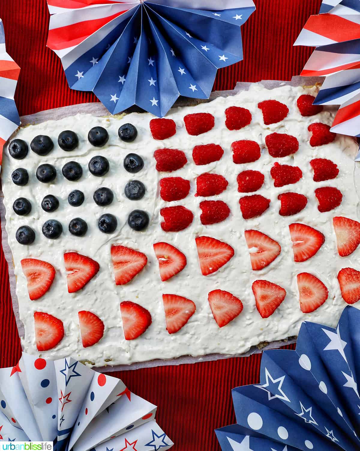 4th of July Fruit Pizza with blueberries, strawberries, raspberries surrounded by red, white, and blue decorations.