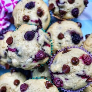several blueberry chocolate chip muffins stacked on top of each other on a plate.