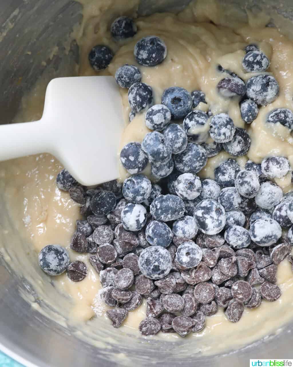 a white spatula gently folding in blueberries and chocolate chips into the batter.