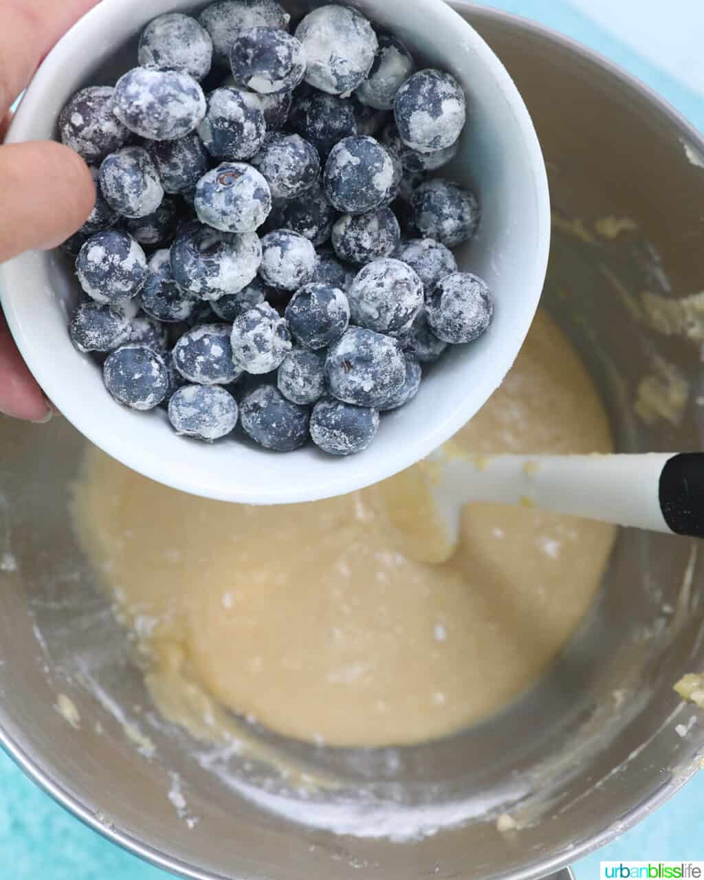 hand holding a bowl of blueberries over cake mix.