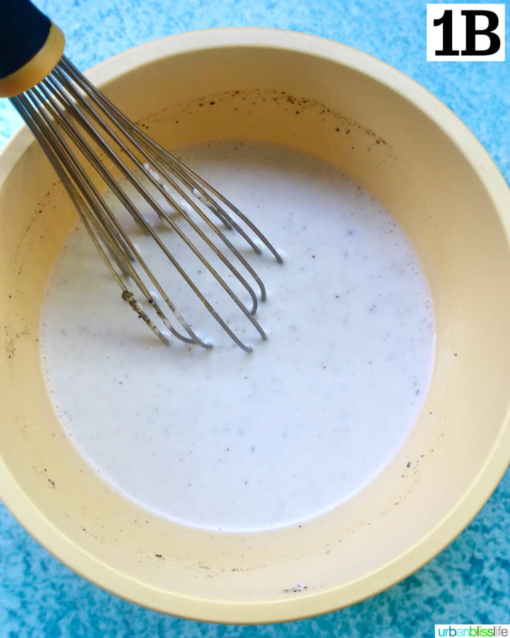 whisking salad dressing in a yellow bowl on top of a blue table.