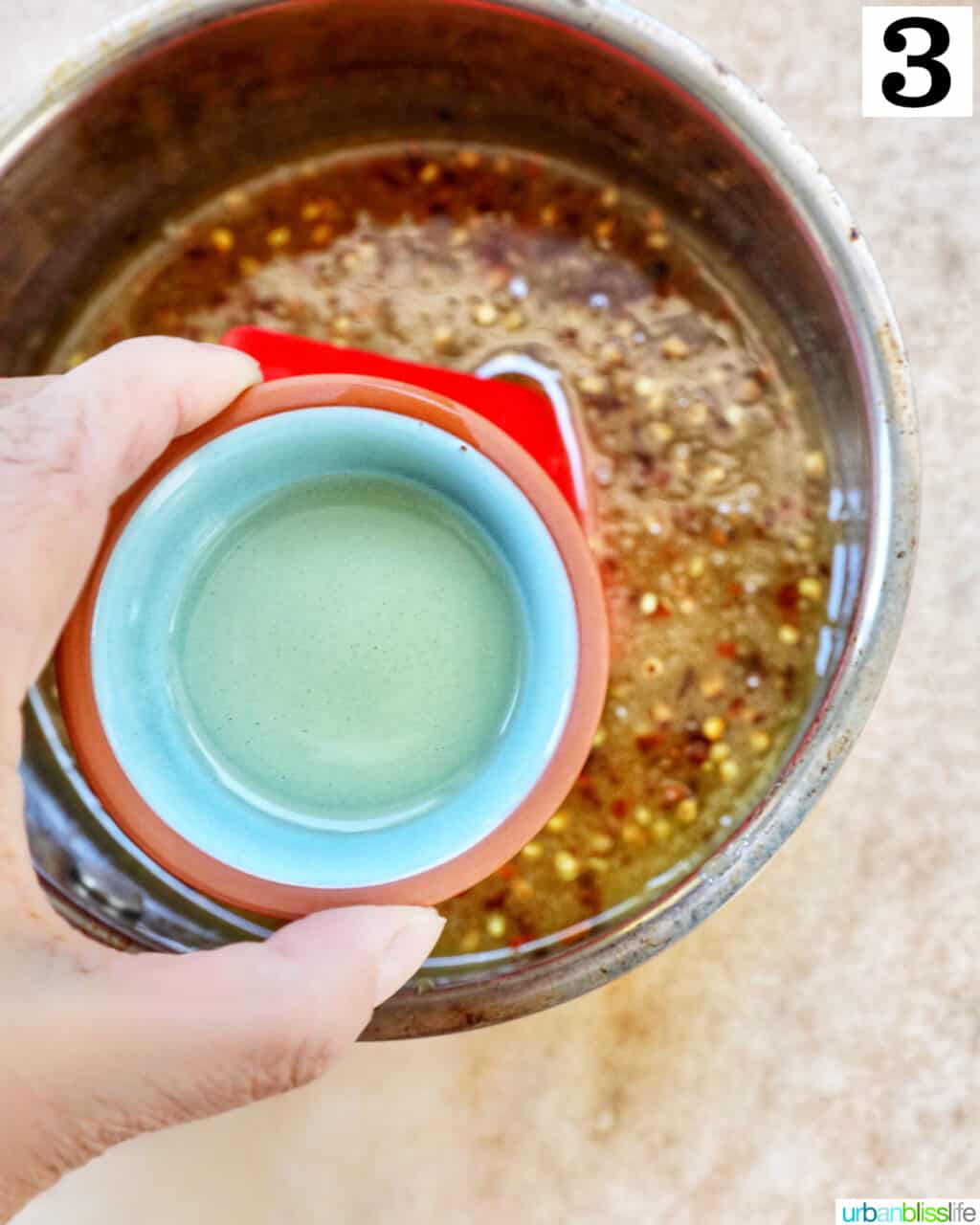 hand holding a small bowl of liquid over hot honey sauce in a saucepan.