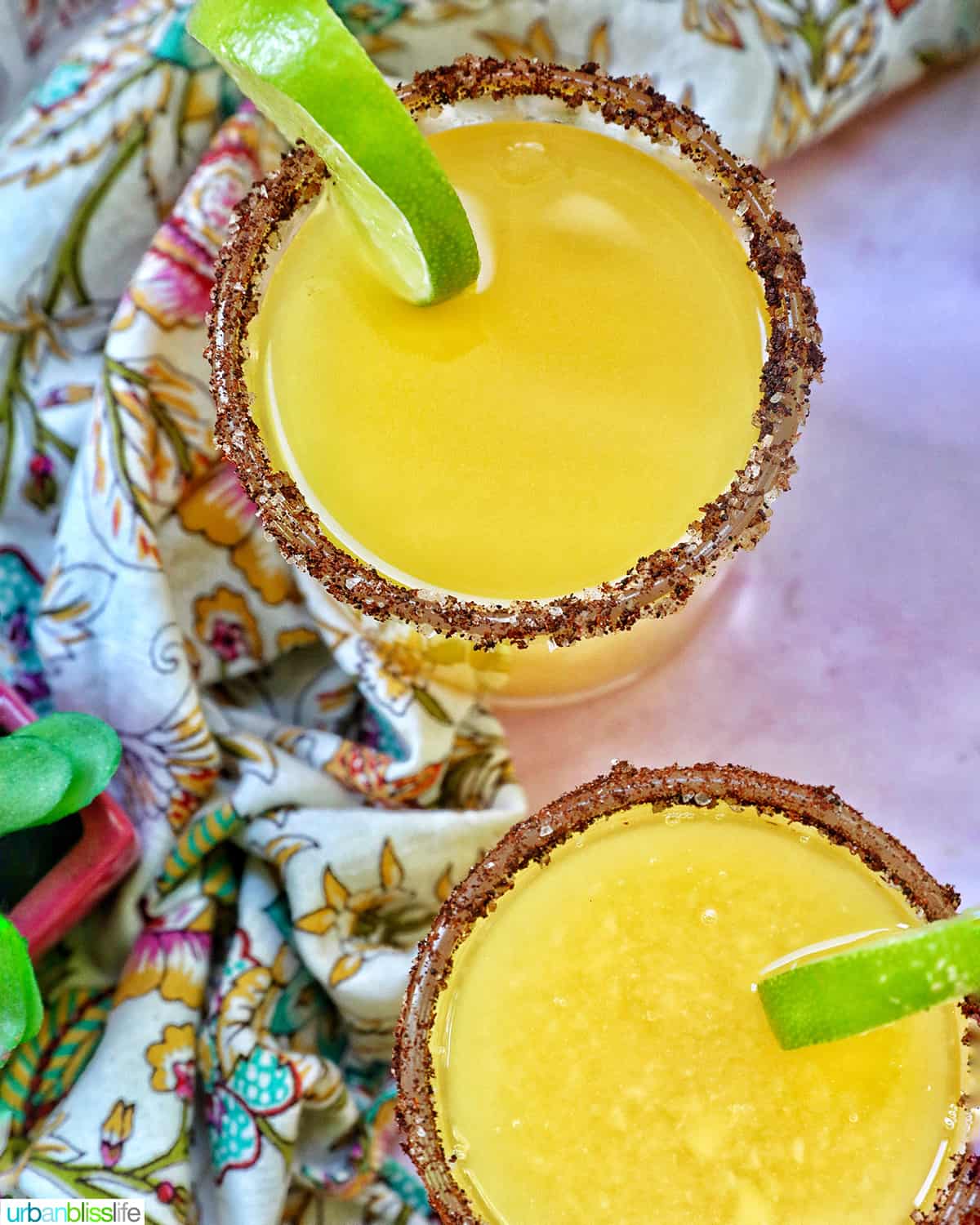two glasses of spicy mango margarita with lime slice garnish and chili powder salt rim.