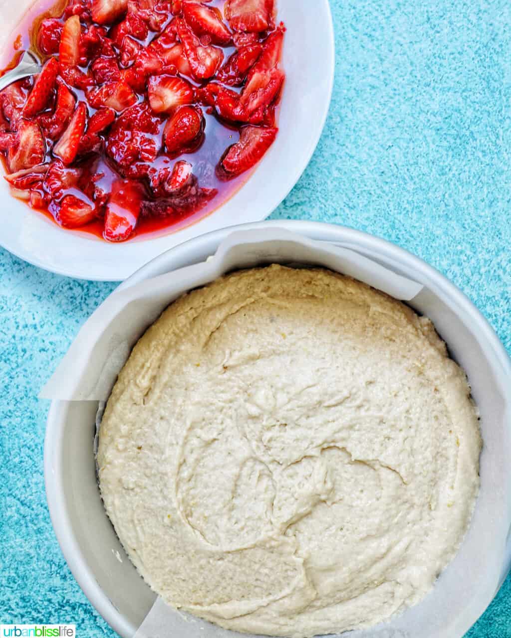 cake pan filled with Strawberry Spoon Cake batter and a white bowl of mashed strawberries above it.