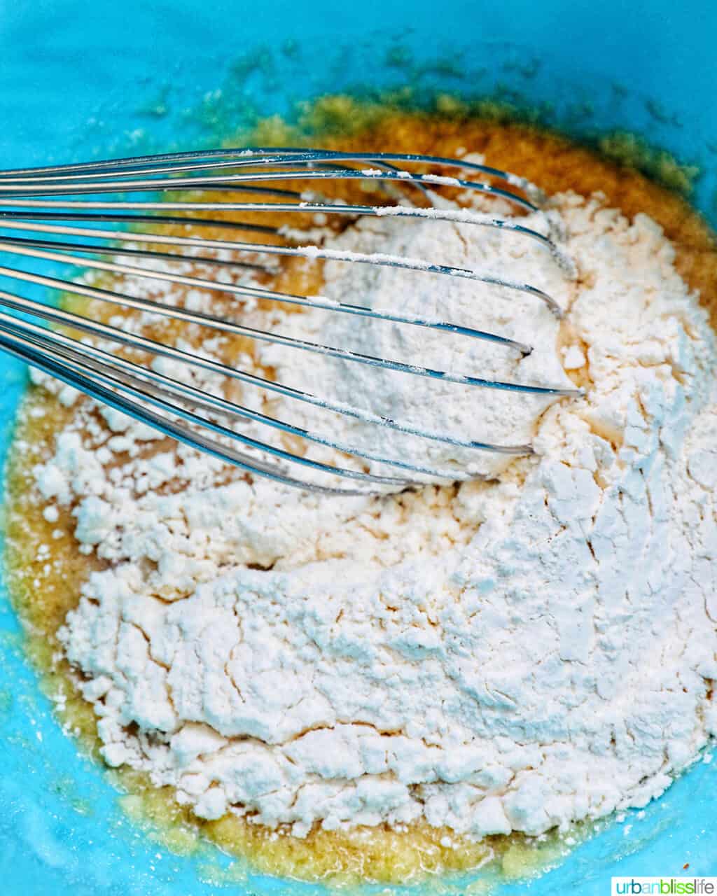 whisk in a blue bowl of wet and dry ingredients.