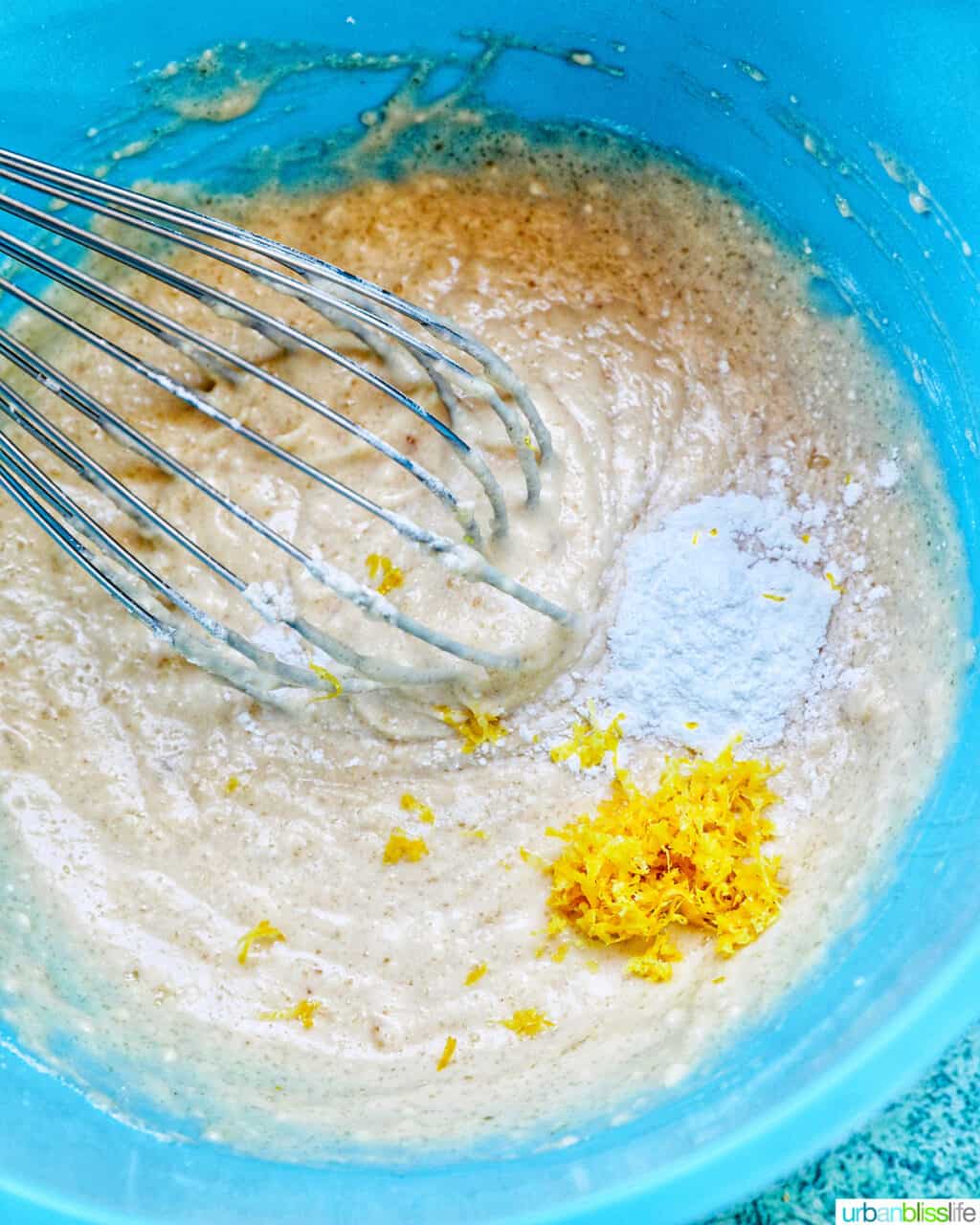 whisk in cake batter with lemon zest in a blue bowl.