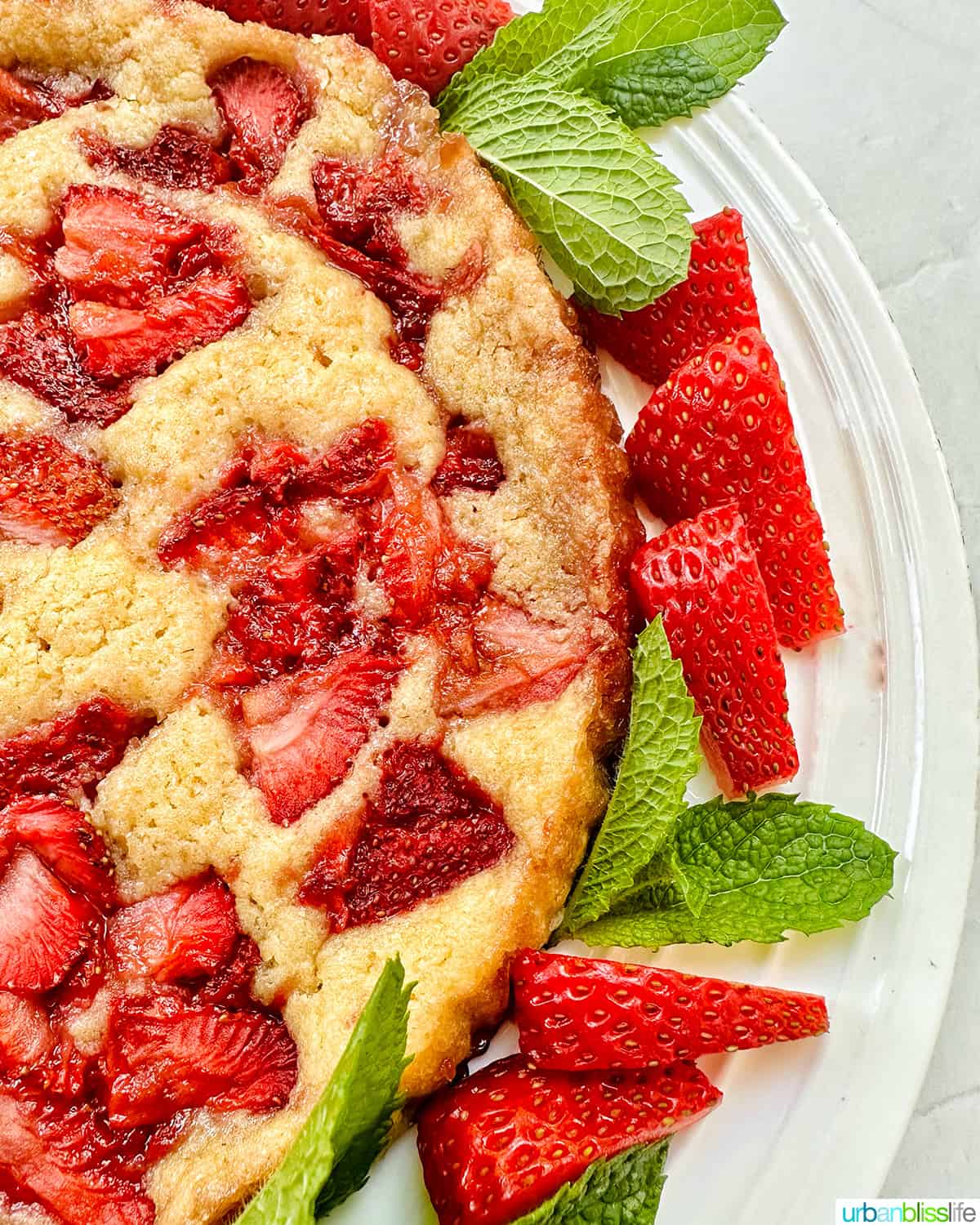half of a Strawberry Spoon Cake with mint leaves and sliced strawberries as garnish on a white plate.