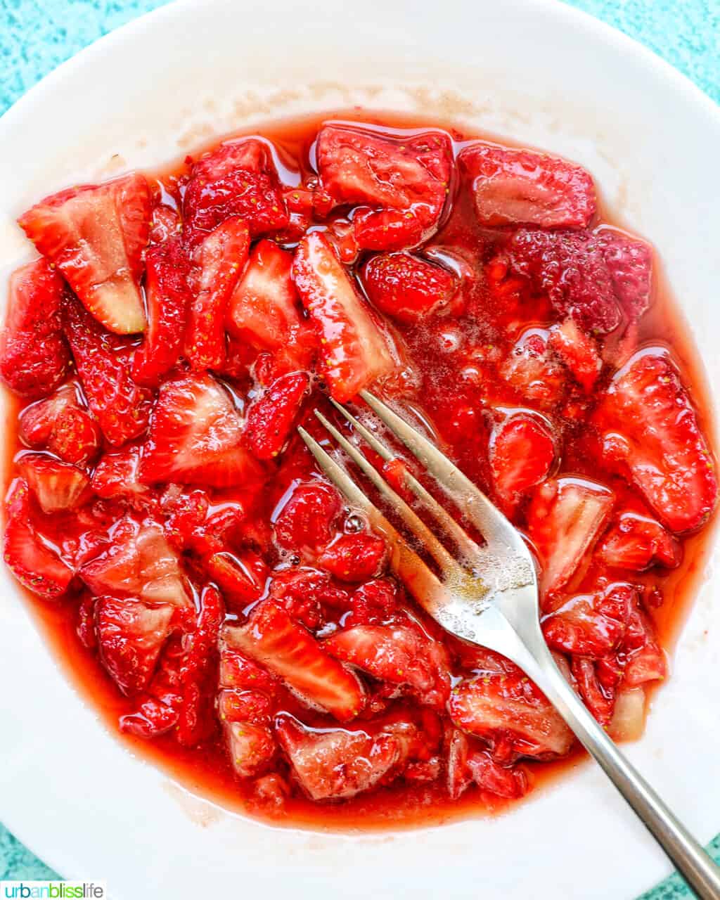 a fork mashing strawberries in a white bowl.