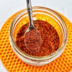 hand holding a spoon in a jar of homemade taco seasoning on a yellow mat.