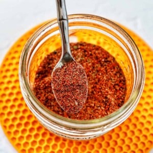 hand holding a spoon in a jar of homemade taco seasoning on a yellow mat.