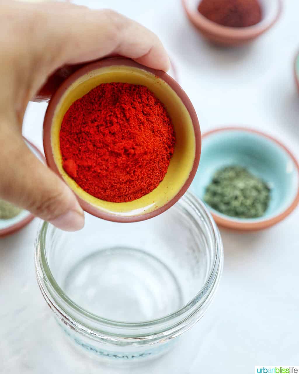 hand holding a bowl of paprika over an empty glass jar.