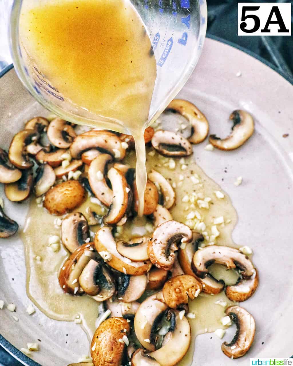 pouring broth over chopped mushrooms cooking in a pan.