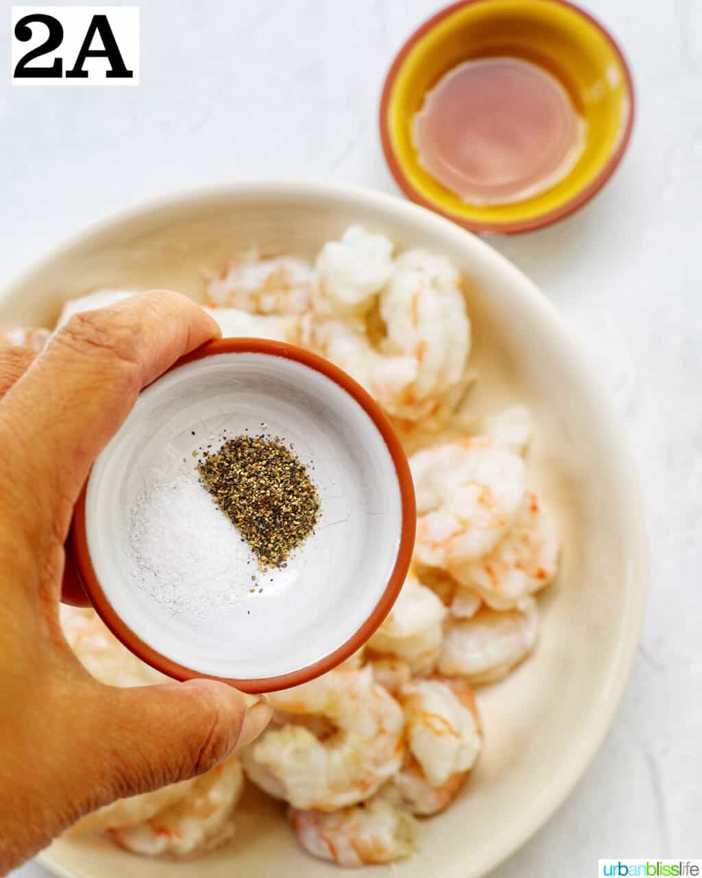hand holding bowl of salt and pepper over bowl of prawns.