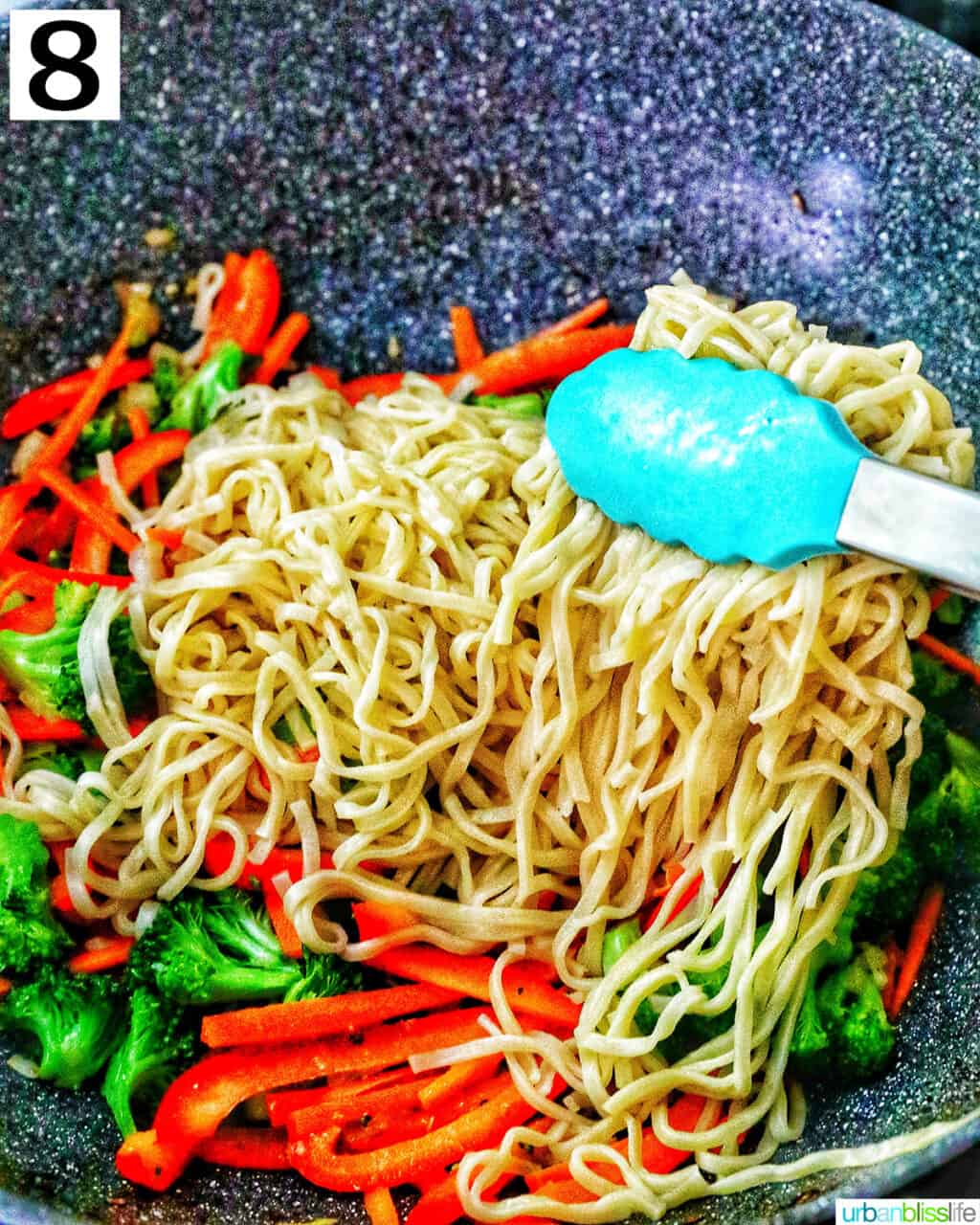 tongs holding prawn chow mein noodles in a wok.