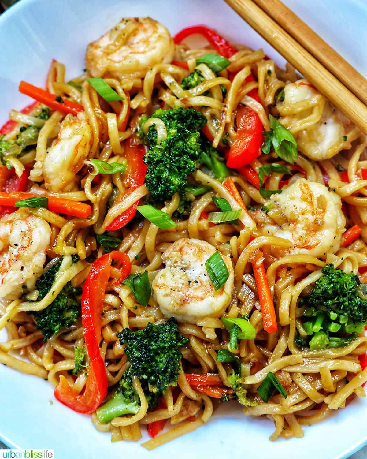 two chopsticks at the top of a while bowl of prawn chow mein noodles.