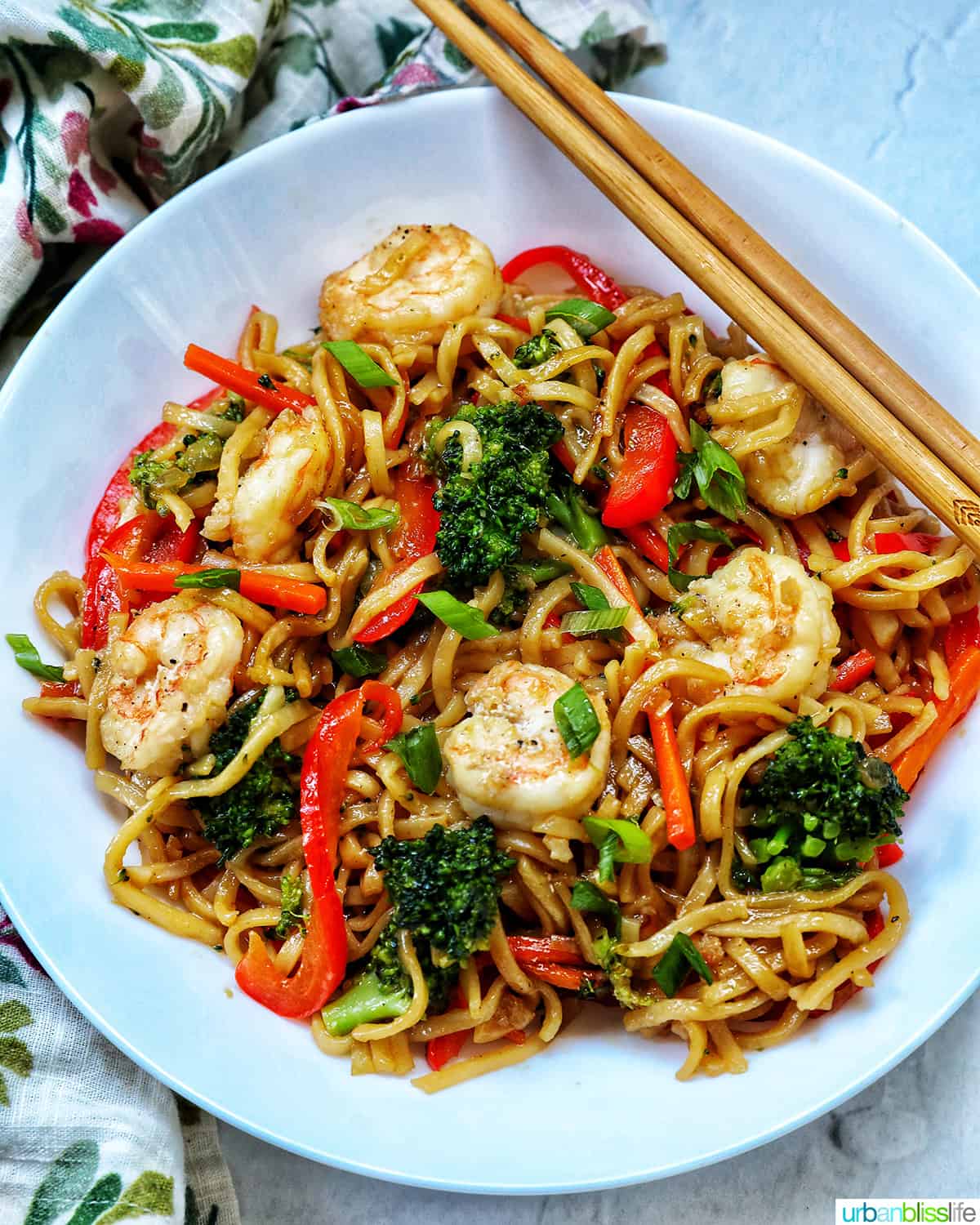 two chopsticks at the top of a while bowl of prawn chow mein noodles.